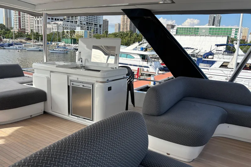 Sixty7 Yacht Photos Pics Luxurious 2023 Lagoon SIXTY 7 yacht interior with modern seating and kitchenette, docked in a marina.