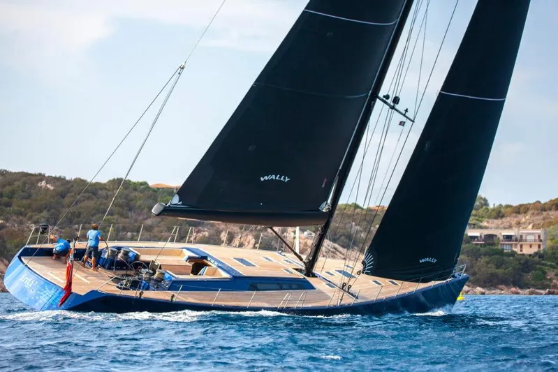  Yacht Photos Pics Sleek 2005 Wally 94' yacht sailing on blue waters near a rocky coastline.