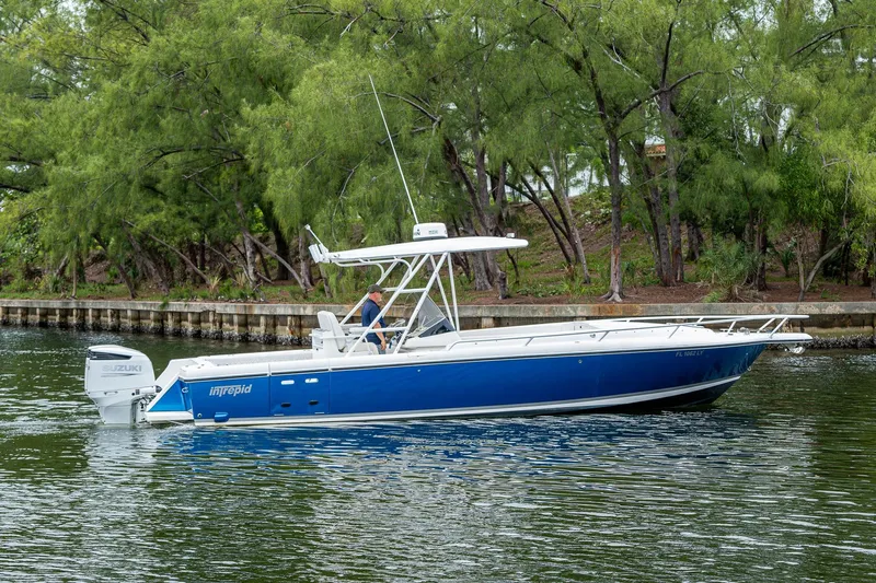  Yacht Photos Pics 2003 Intrepid 323 boat with Suzuki engine on calm water near trees.