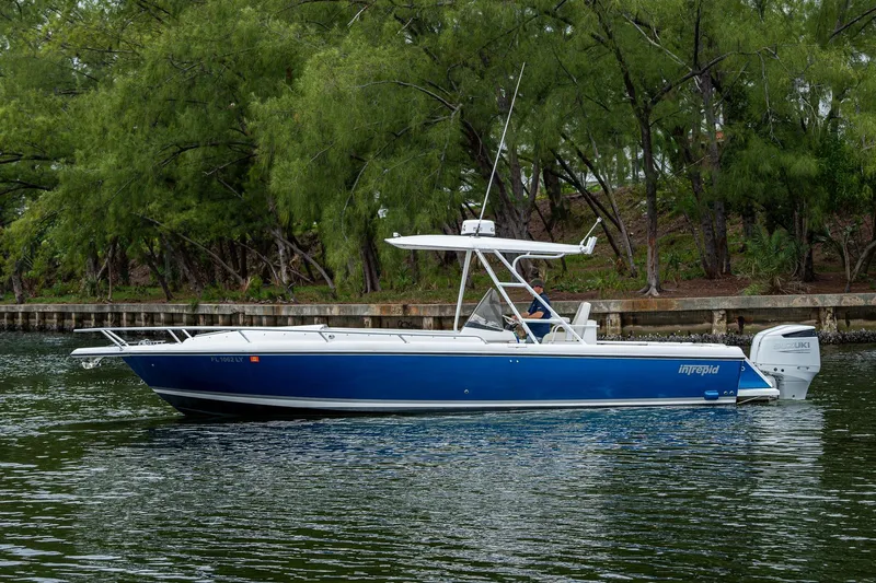  Yacht Photos Pics Blue 2003 Intrepid 323 boat cruising on a calm waterway, surrounded by lush greenery.