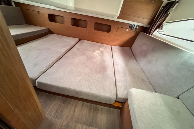  Yacht Photos Pics 2024 Beneteau Antares 11 interior cabin with gray cushions and wooden accents.