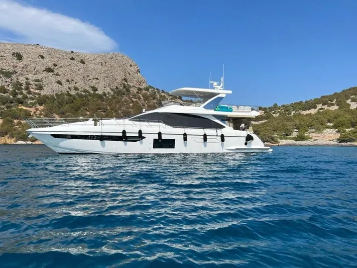Goldinia Yacht Photos Pics 2021 Azimut 72 yacht cruising in clear blue waters near rocky coastline.