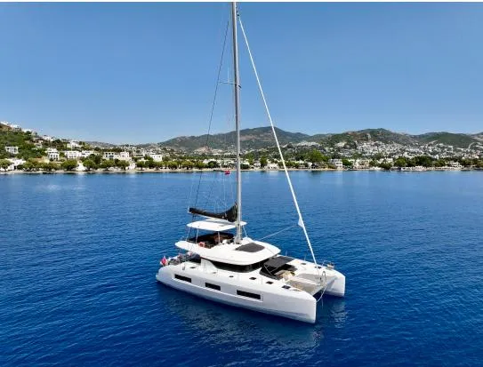  Yacht Photos Pics 2023 Lagoon 55 catamaran sailing on clear blue waters near a coastal town.