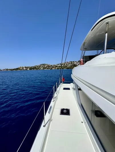  Yacht Photos Pics 2023 Lagoon 55 yacht sailing on clear blue waters near a coastal landscape.