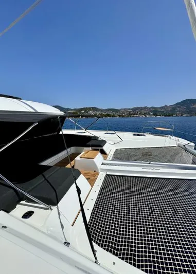  Yacht Photos Pics 2023 Lagoon 55 yacht with netted deck, scenic ocean view, and distant hills.