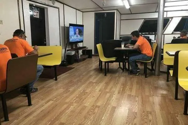 Southern Comfort Yacht Photos Pics Workers in orange shirts relax in a break room with a TV and yellow seating.