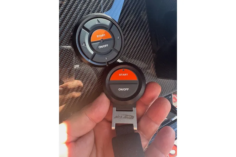  Yacht Photos Pics Hand holding Nor-Tech 390 Sport Center Console 2025 start button on carbon fiber background.