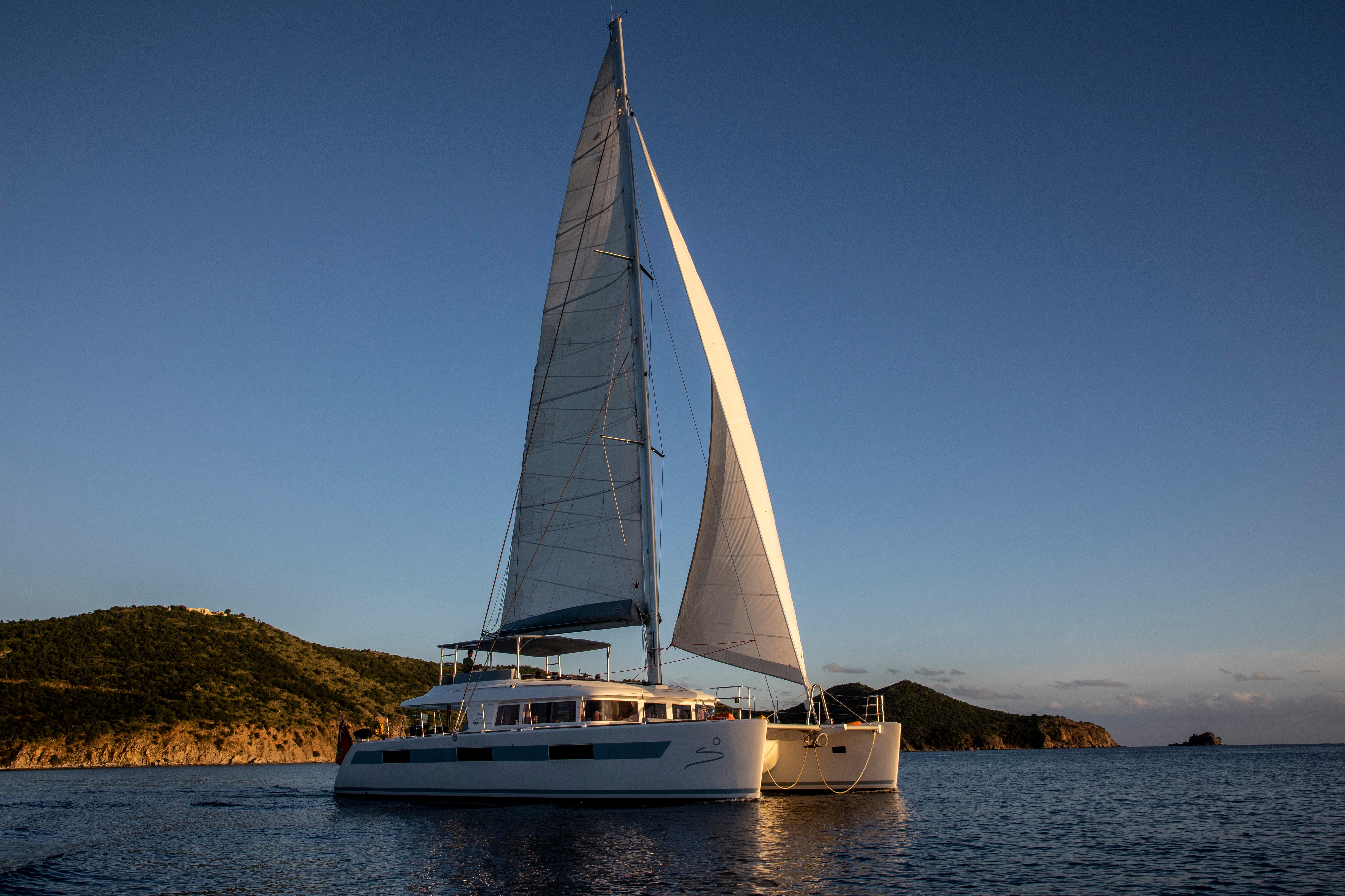 2014 Lagoon 620 catamaran sailing at sunset near scenic coastline.