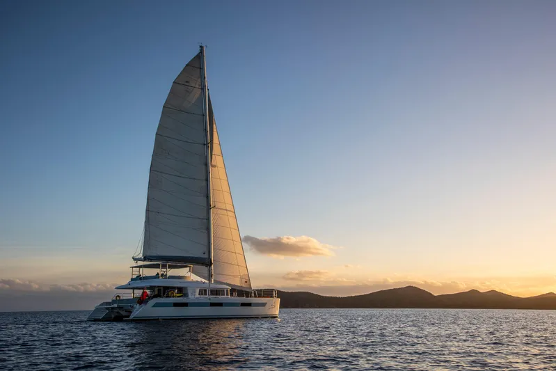 Nomada Yacht Photos Pics Lagoon 620 catamaran sailing at sunset, 2014 model, on calm ocean waters.