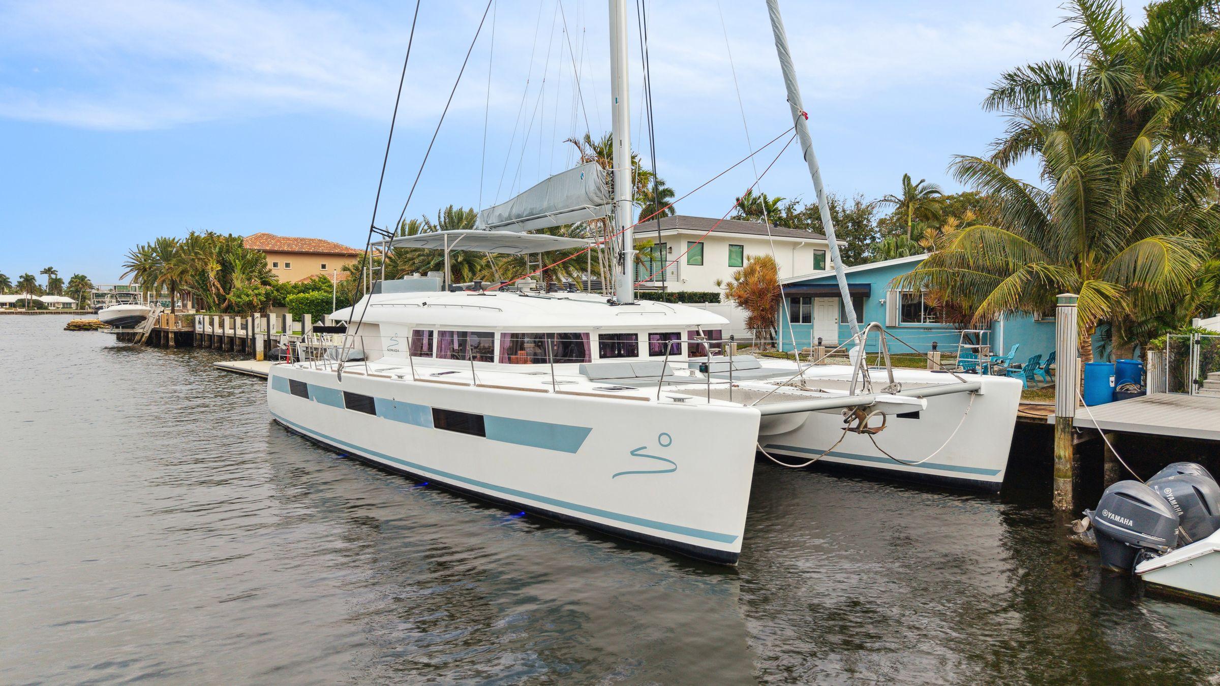Lagoon 620 catamaran, 2014 model, docked by palm trees and waterfront homes.