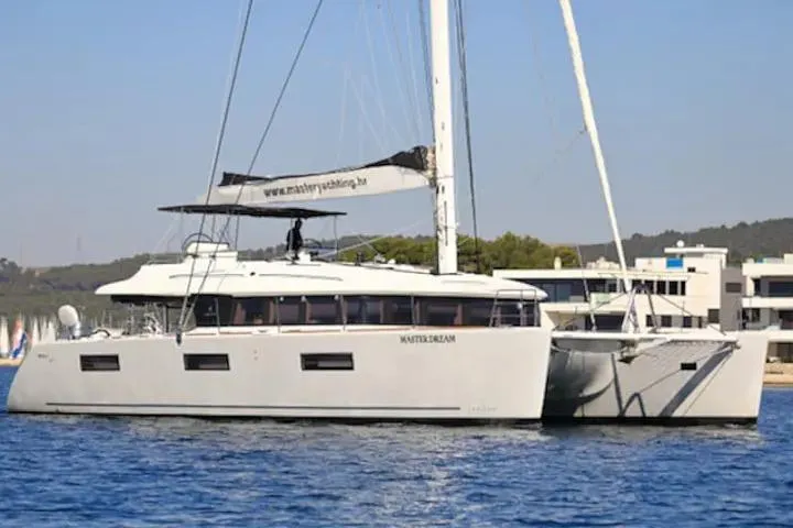 Masterdream Yacht Photos Pics 2018 Lagoon 620 Esense catamaran sailing on calm waters near a coastal area.