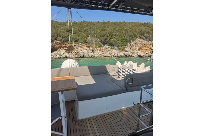  Yacht Photos Pics Luxurious Lagoon 560 S2 yacht deck with cushions, overlooking serene turquoise waters and rocky shoreline.