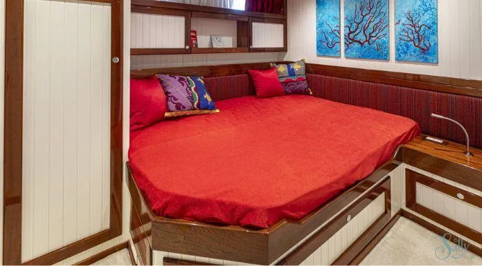 Sally Yacht Photos Pics Cozy cabin interior with red bedding, colorful pillows, and ocean-themed artwork on a 1959 Burger 60 yacht.