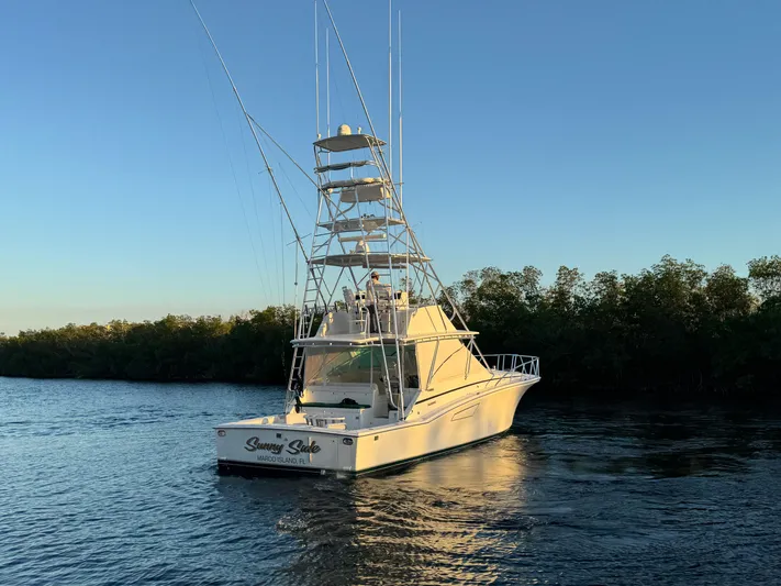 Yacht Photos Pics Cabo 45 Express 1999 yacht on calm water at sunset, surrounded by trees.