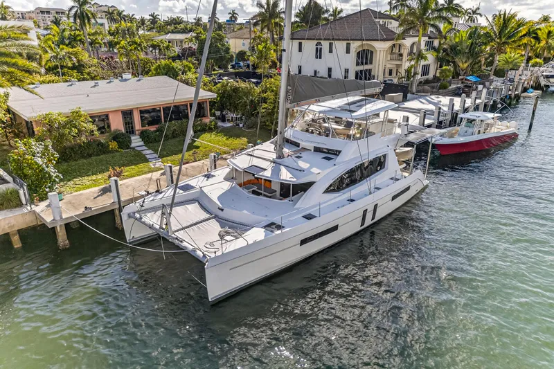  Yacht Photos Pics 2019 Leopard 58 catamaran docked by waterfront homes, surrounded by lush greenery.