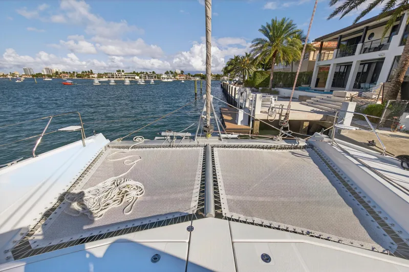  Yacht Photos Pics 2019 Leopard 58 catamaran docked by waterfront homes, featuring spacious deck and netting.