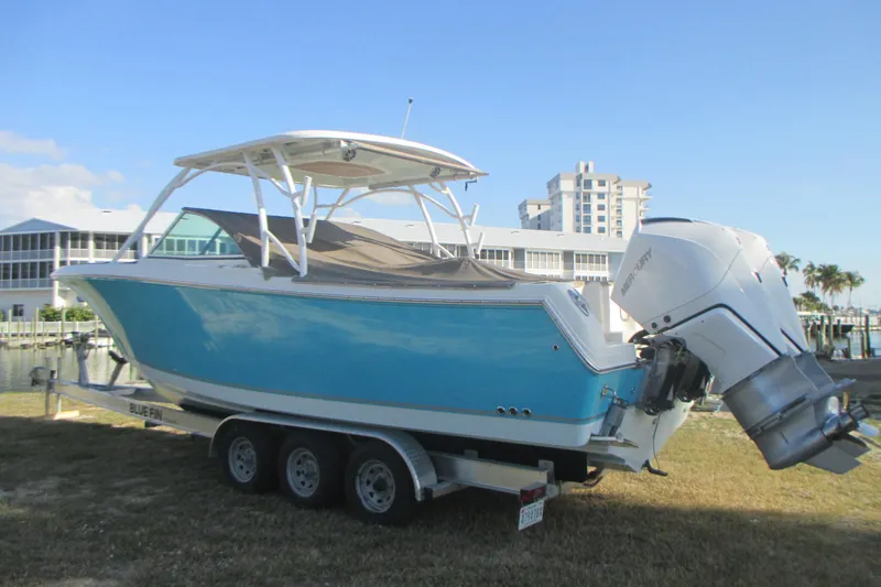  Yacht Photos Pics 2019 Sailfish 325 DC boat on trailer, blue hull, Mercury outboard, waterfront background.