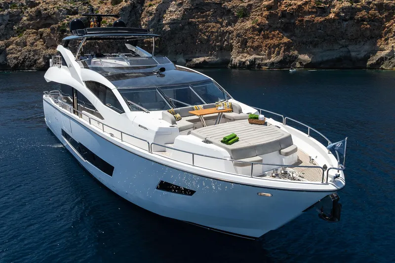 Seawater Yacht Photos Pics Luxurious 2019 Sunseeker 86 Yacht cruising in clear blue waters near rocky coastline.