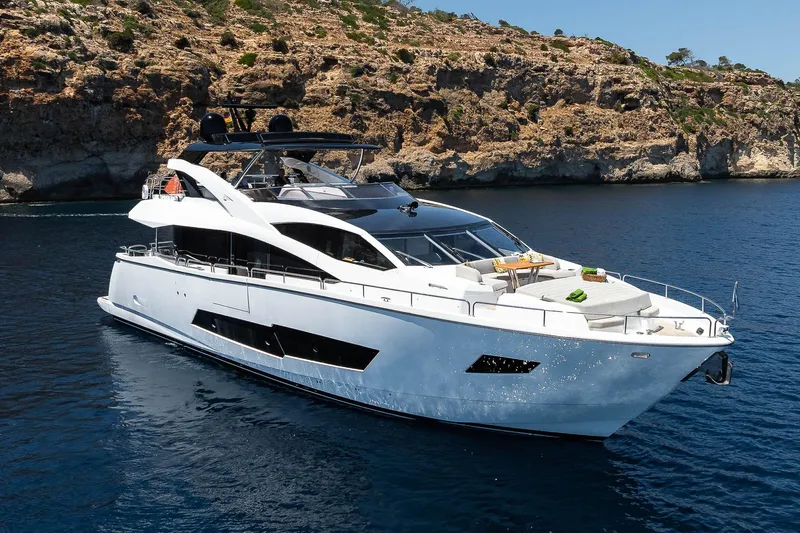 Seawater Yacht Photos Pics Luxurious 2019 Sunseeker 86 Yacht cruising in serene blue waters near rocky coastline.