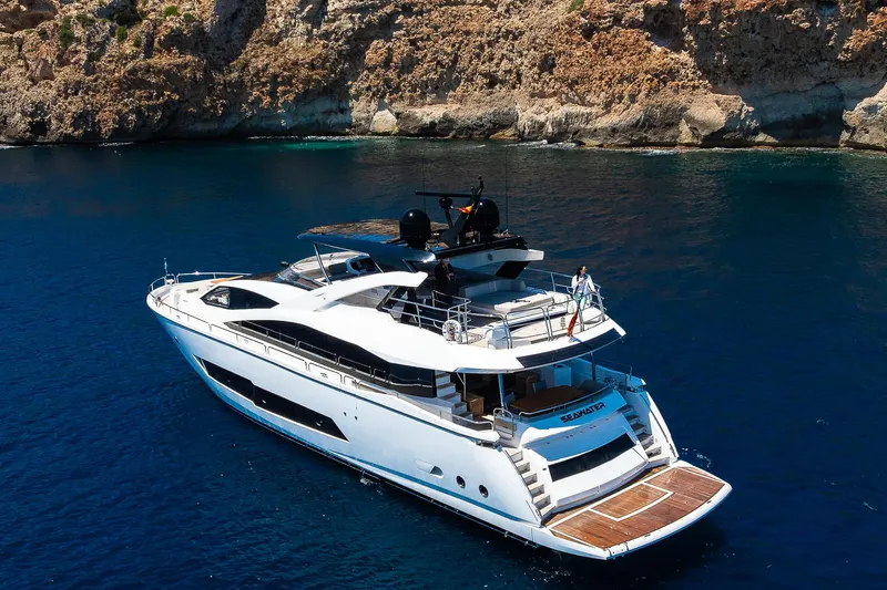 Seawater Yacht Photos Pics 2019 Sunseeker 86 Yacht cruising in clear blue waters near rocky coastline.