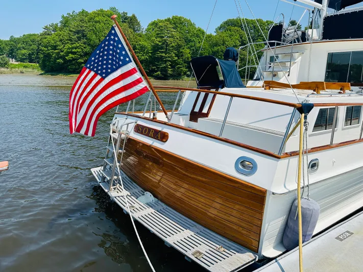 Sora Yacht Photos Pics 1998 Grand Banks 49 Classic yacht with American flag, docked by lush greenery.