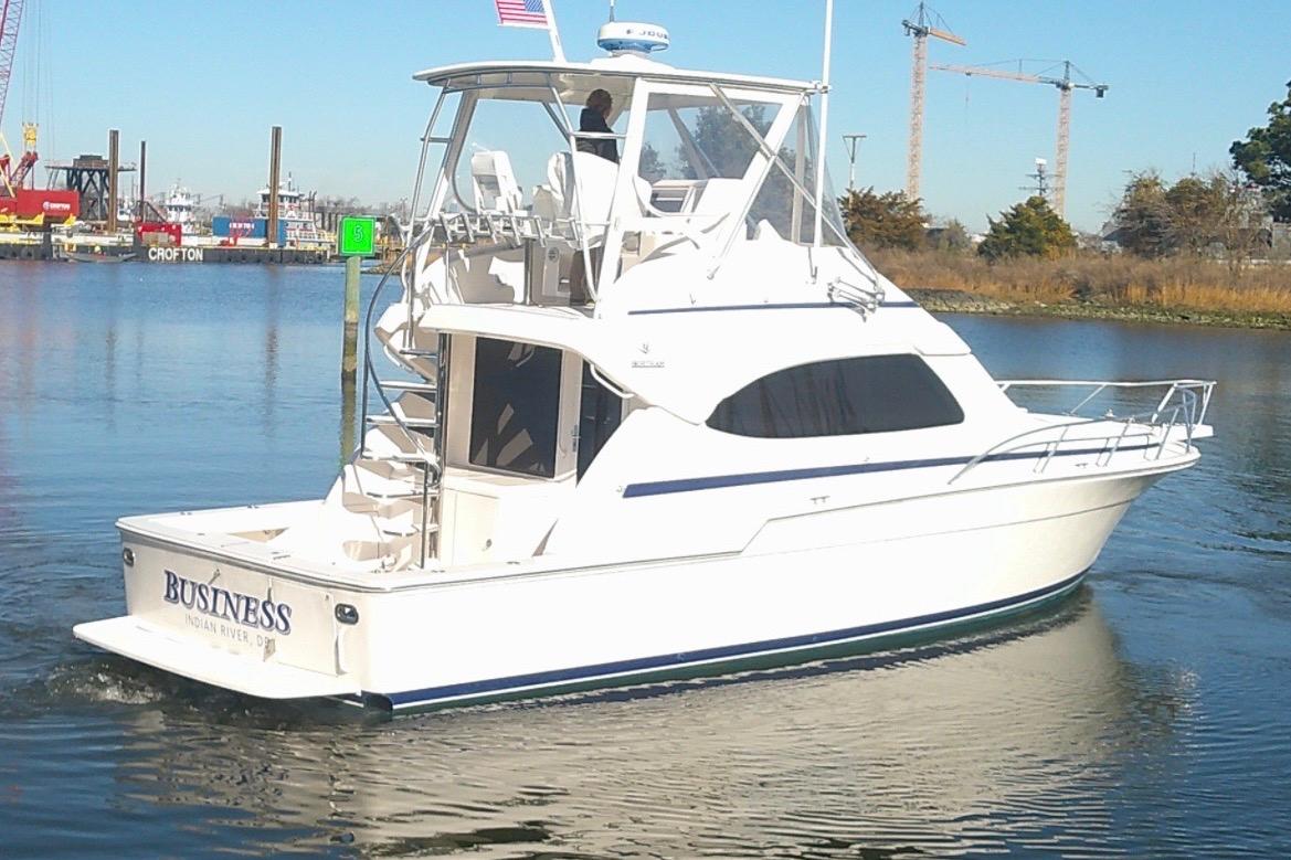 2005 Bertram 390 Convertible yacht cruising on a calm river with industrial backdrop.
