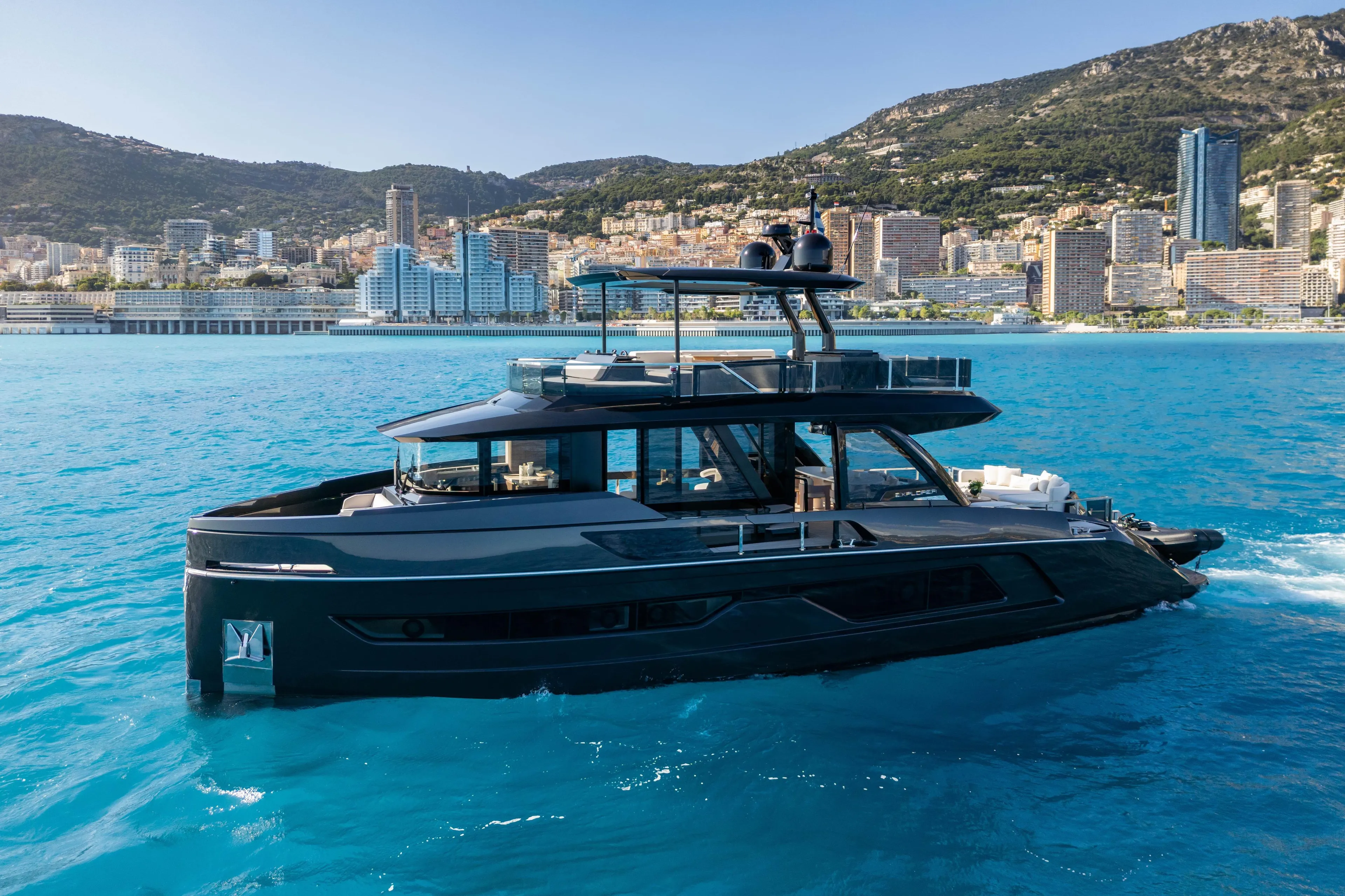 Luxurious 2025 Explorer 62 yacht cruising in vibrant blue waters near a coastal cityscape.