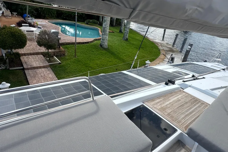 Grand Crew Yacht Photos Pics 2019 Fountaine Pajot 47 yacht with solar panels, docked near a poolside garden.