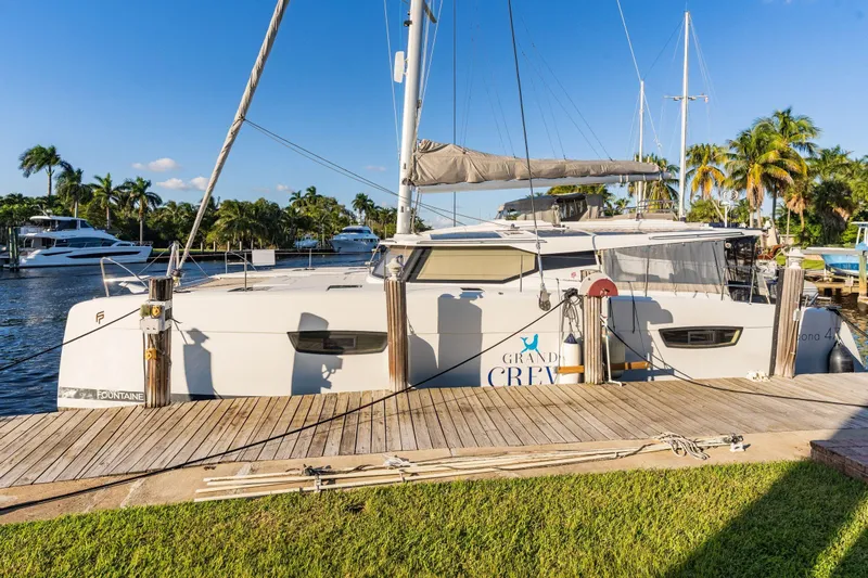 Grand Crew Yacht Photos Pics 2019 Fountaine Pajot 47 catamaran docked, surrounded by palm trees and clear blue sky.