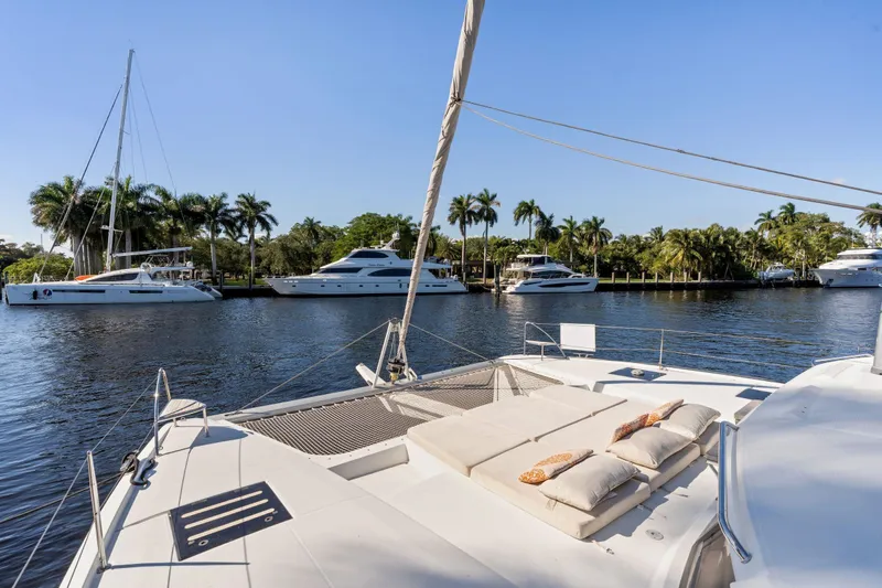 Grand Crew Yacht Photos Pics 2019 Fountaine Pajot 47 catamaran on tranquil waterway with palm trees and yachts.