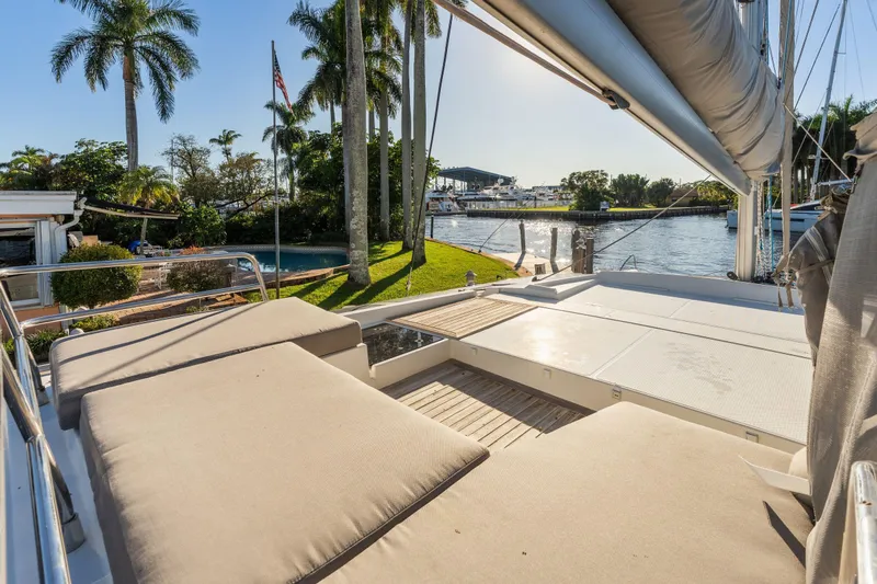 Grand Crew Yacht Photos Pics Luxurious 2019 Fountaine Pajot 47 catamaran with sunbathing area, docked by palm trees.