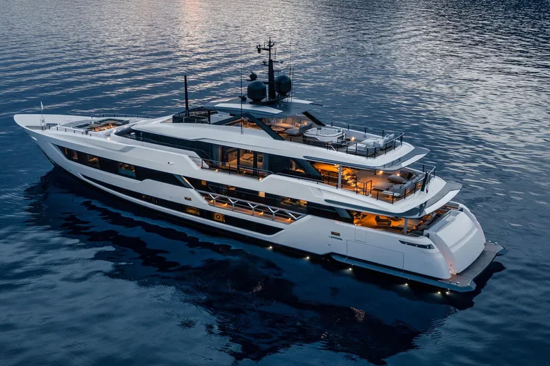  Yacht Photos Pics Luxurious 2022 Custom Line 140' yacht illuminated on serene water at dusk.