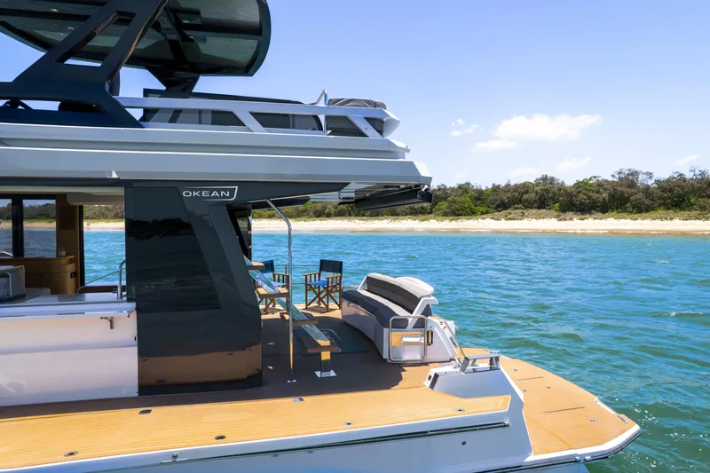 Da Mare Yacht Photos Pics Luxury 2023 OKEAN 52 yacht on serene blue waters near a sandy shoreline.