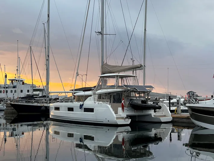 Vela Yacht Photos Pics 2021 Lagoon 46 catamaran docked at sunset, reflecting on calm water.