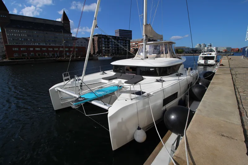 Vela Yacht Photos Pics 2021 Lagoon 46 catamaran docked in urban marina under clear blue sky.