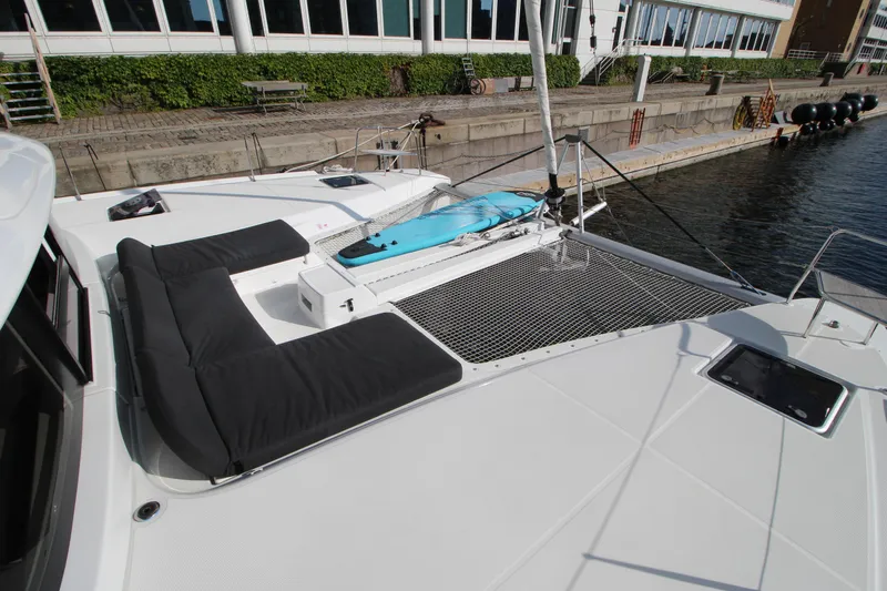 Vela Yacht Photos Pics 2021 Lagoon 46 catamaran with spacious deck, black seating, and paddleboard, docked at marina.