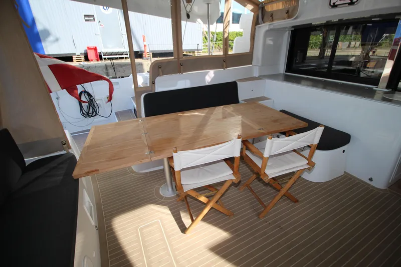 Vela Yacht Photos Pics Outdoor seating area on 2021 Lagoon 46 catamaran with wooden table and chairs.