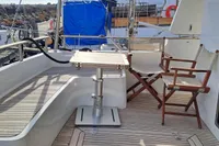 2008 Beneteau Swift Trawler 52 deck with seating and table, docked by rocky shoreline.