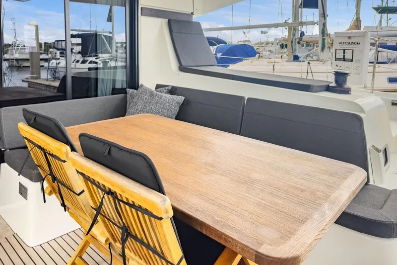 Sweet Sweet Life Yacht Photos Pics Outdoor seating area on 2020 Lagoon 42 catamaran with wooden table and cushioned chairs.