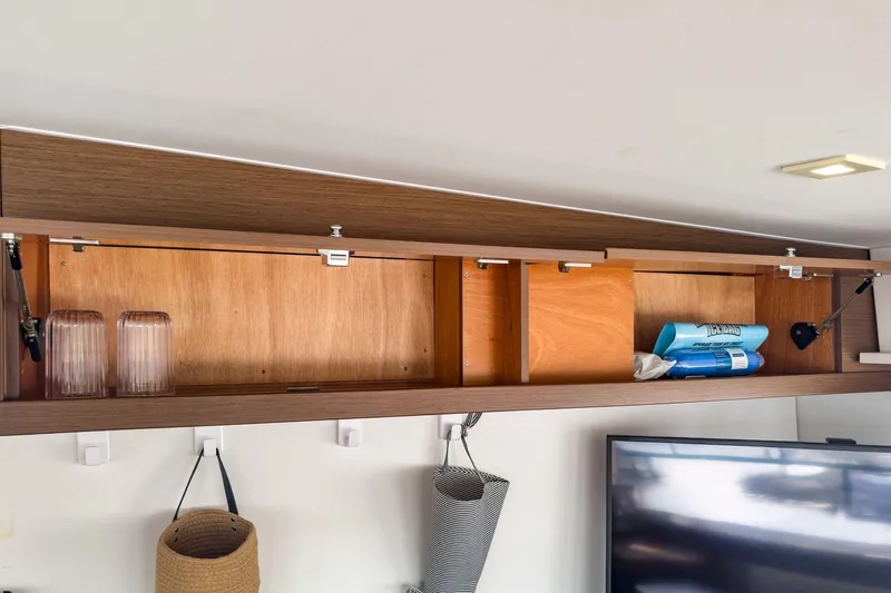 Sweet Sweet Life Yacht Photos Pics Open wooden cabinet in Lagoon 42 yacht, displaying glasses and cleaning supplies.