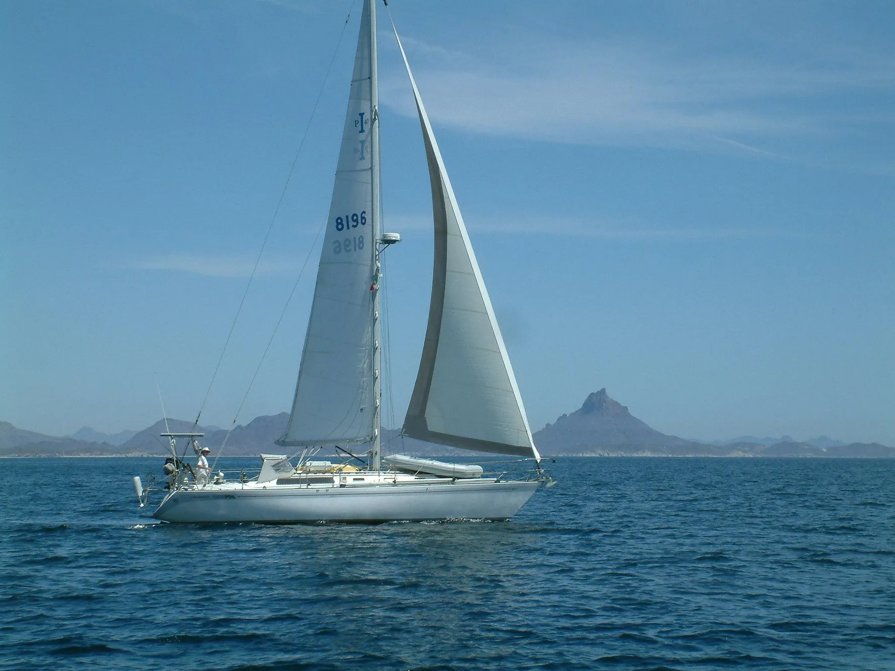 Sailboat Islander IP Peterson 40, 1979, sailing on calm sea with mountain backdrop.