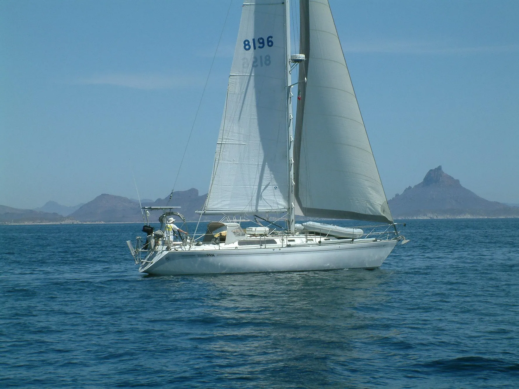 Sailing yacht Islander IP Peterson 40, 1979, on calm sea with mountainous background.