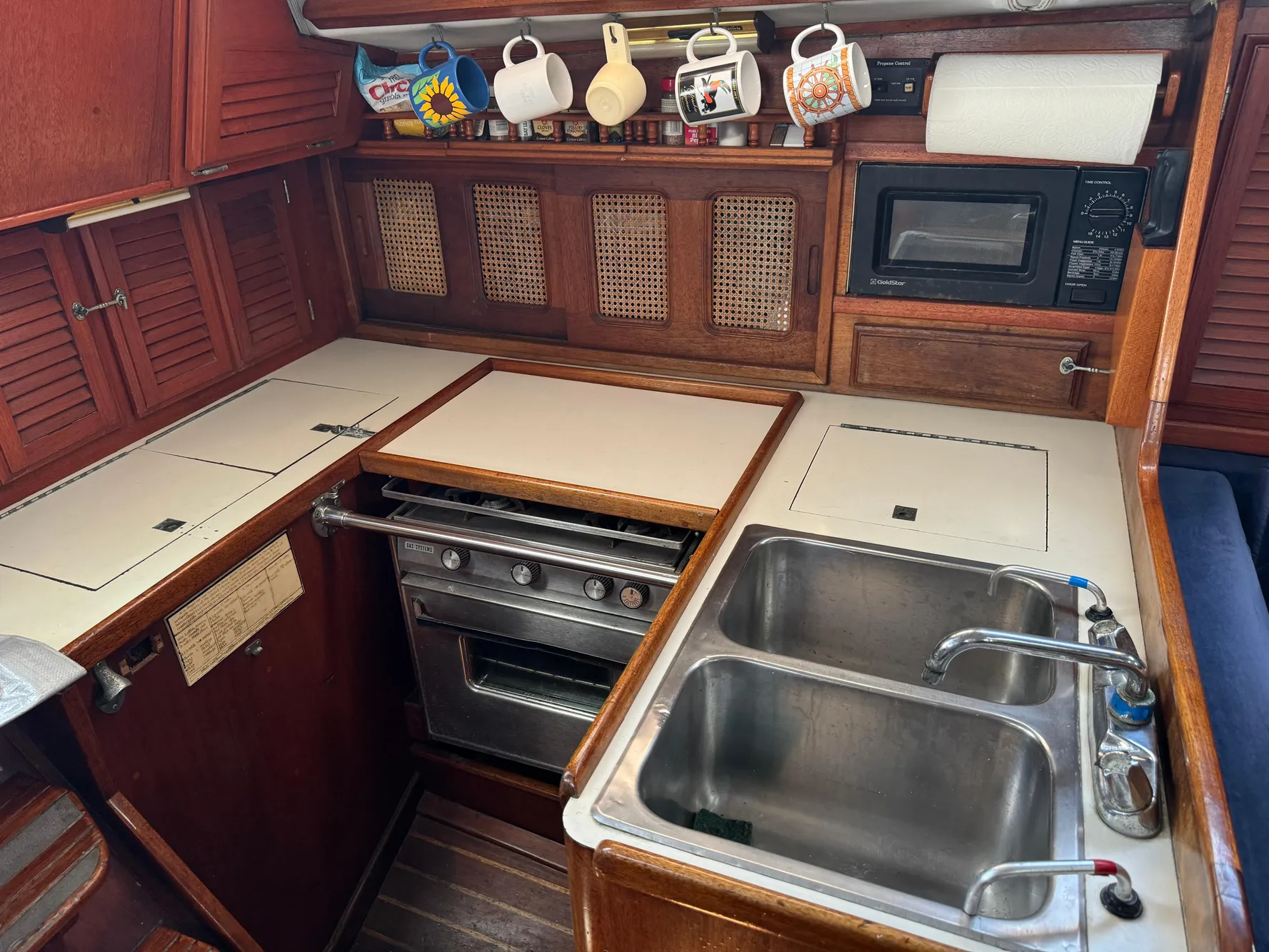 1979 Islander IP Peterson 40 yacht kitchen with stove, sink, microwave, and hanging mugs.