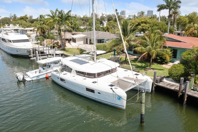 Curvy Mermaid Yacht Photos Pics 2017 Lagoon 42 catamaran docked by tropical waterfront homes, surrounded by lush greenery.