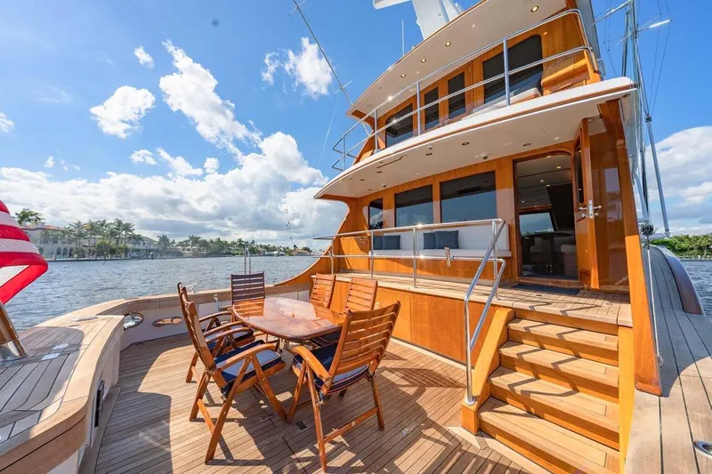 Catch Yacht Photos Pics Luxurious 1984 Feadship Yacht Fish with wooden deck and outdoor seating, docked by a scenic waterfront.