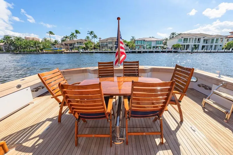 Catch Yacht Photos Pics Outdoor dining area on 1984 Feadship Yacht Fish, featuring wooden chairs and table, with waterfront view.