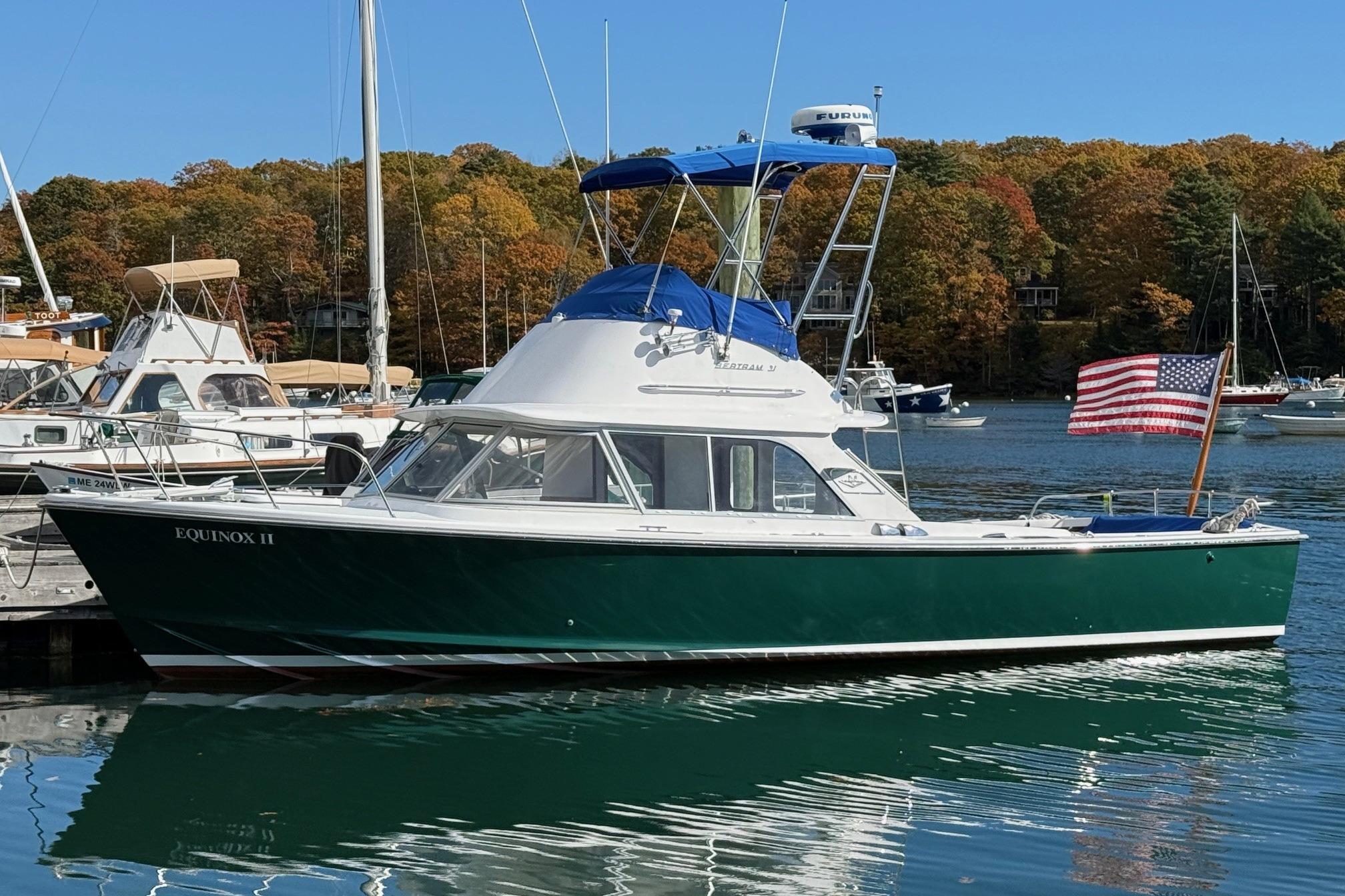 1963 Bertram 31 Flybridge Cruiser docked, displaying American flag, with autumn trees in background.
