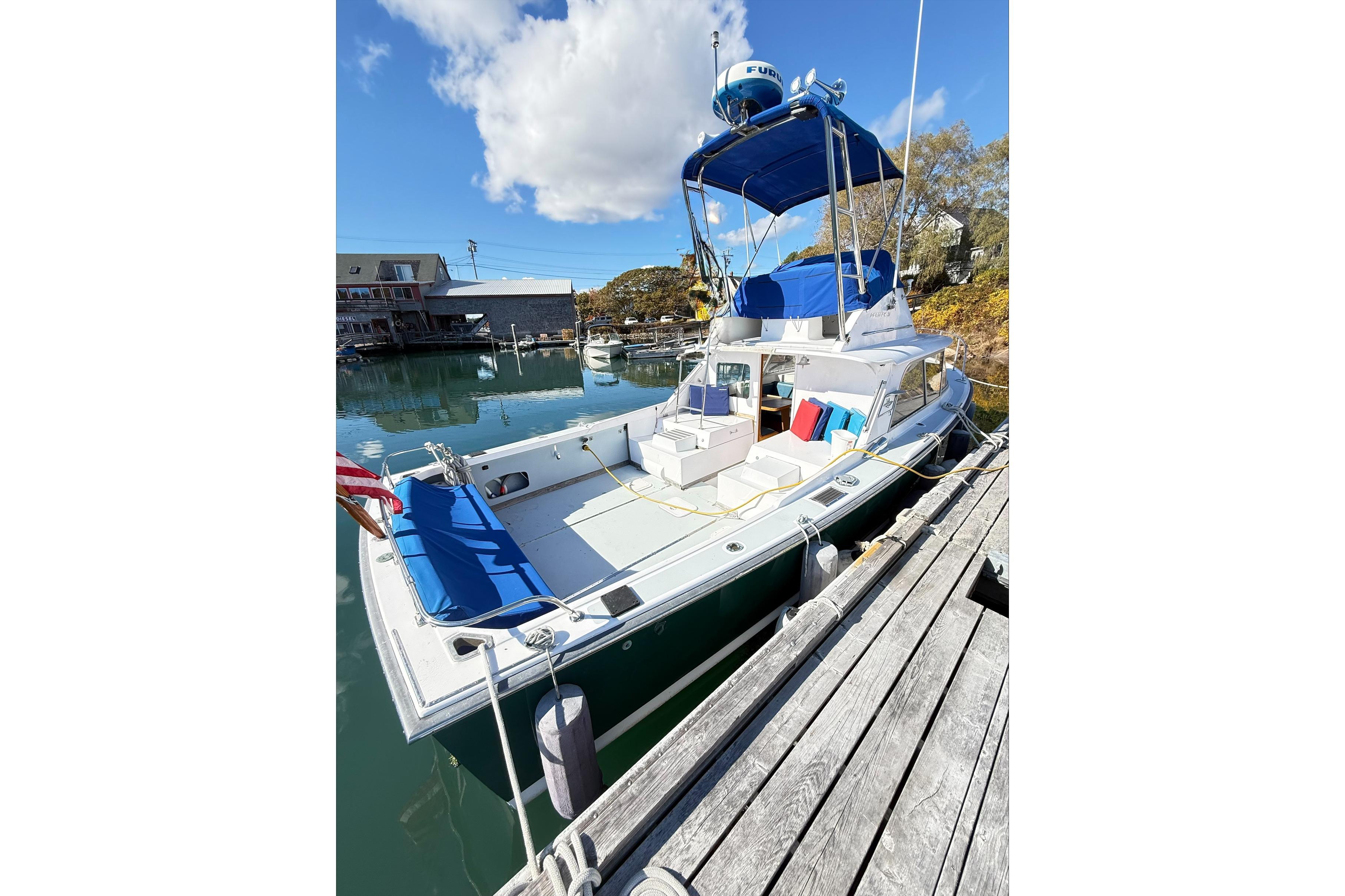 1963 Bertram 31 Flybridge Cruiser docked, featuring blue canopy and seating, under clear sky.