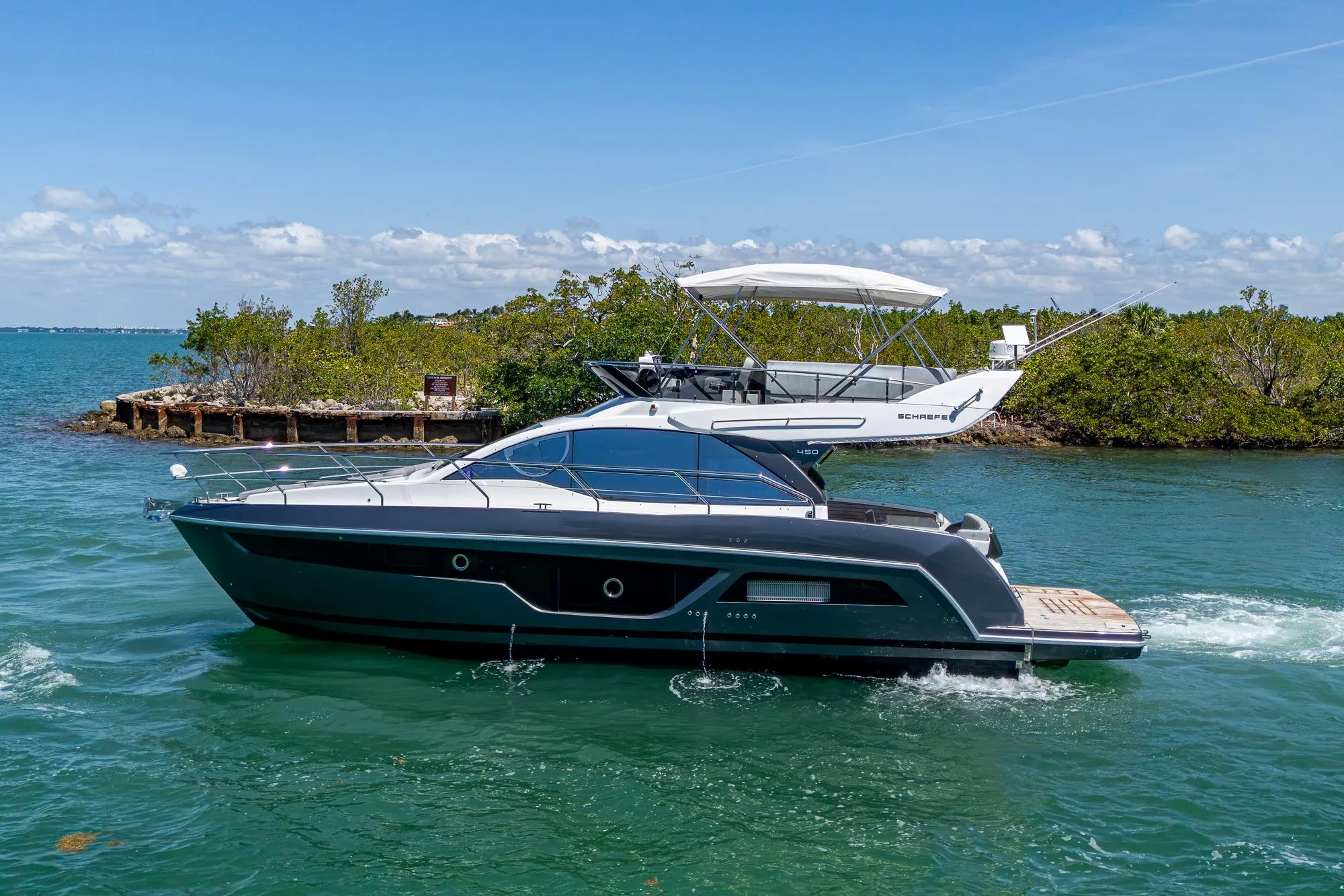 2023 Schaefer 450 yacht cruising on clear blue water near lush greenery.