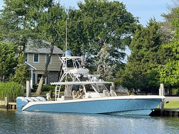  Yacht Photos Pics 2019 Everglades 435 CC boat docked by a waterfront home, surrounded by lush greenery.